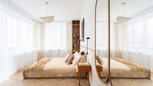Een moderne slaapkamer met een groot bed, nachtkastjes, een spiegel en een boekenplank.