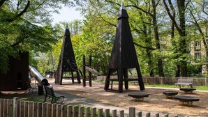 Un parco con giochi per bambini, panchine e una recinzione in legno.