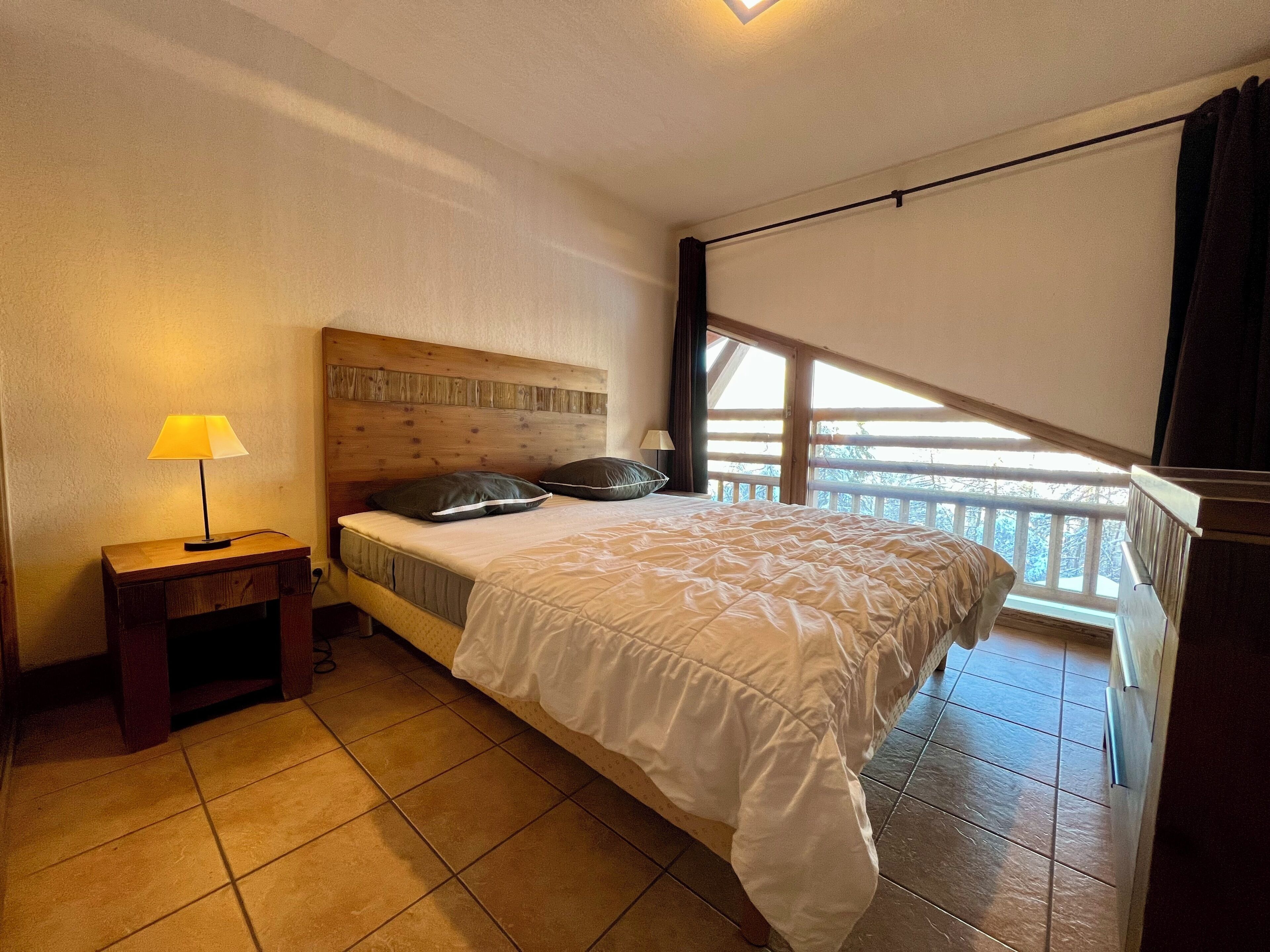 Ein Schlafzimmer mit einem Bett, einem Nachttisch, einer Lampe, einem Fenster mit Blick und einem Balkon.