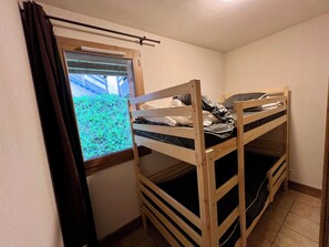 Ein kleines Zimmer mit zwei Etagenbetten, einem Fenster mit Blick auf Grünflächen und einem Vorhang.