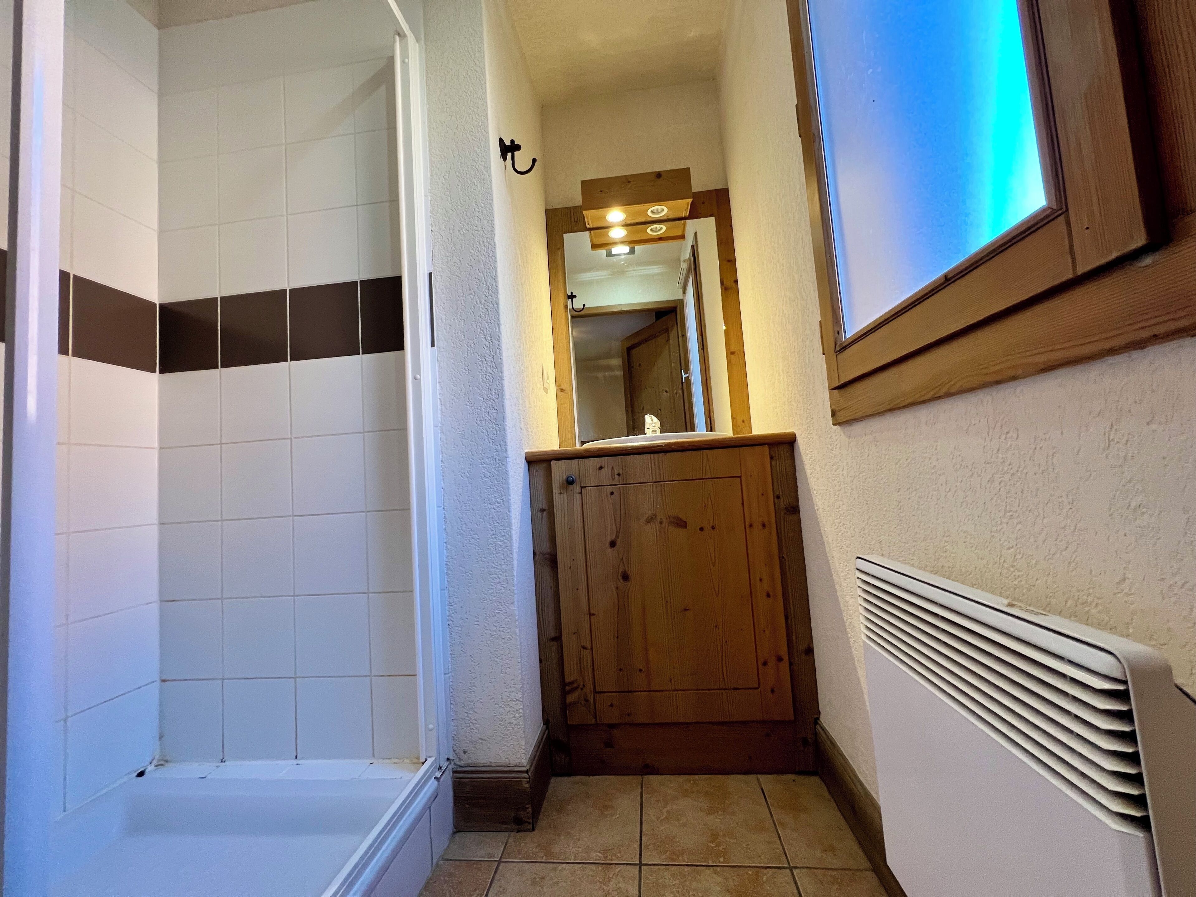 A bathroom with a shower, a wooden cabinet, a mirror, and a radiator.