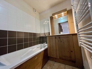 Een badkamer met een wit bad, houten kastjes en een spiegel boven de wastafel.