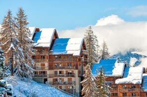 Ein mehrstöckiges Holzchalet mit Balkonen, umgeben von schneebedeckten Bäumen und Bergen.