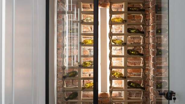 Una pared de ladrillo con una estantería para vinos que contiene varias botellas.