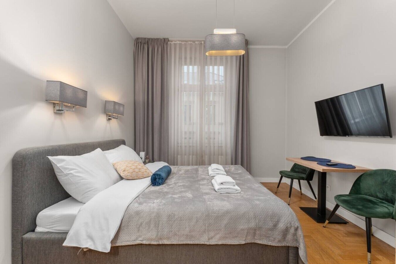 Una habitación de hotel moderna con cama, escritorio, silla, televisor y ventana con cortinas.