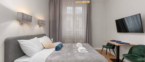 Una habitación de hotel moderna con cama, escritorio, silla, televisor y ventana con cortinas.