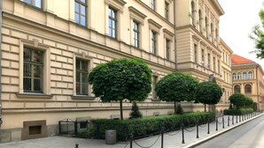 Ein Gebäude mit einer symmetrischen Fassade, großen Fenstern und einem gepflasterten Bürgersteig mit einer Kettenbarriere.