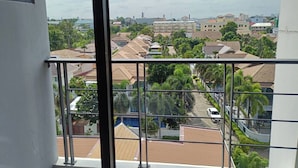 Zona residencial con varias casas, cielo despejado y vista por una ventana con barandilla de balcón.