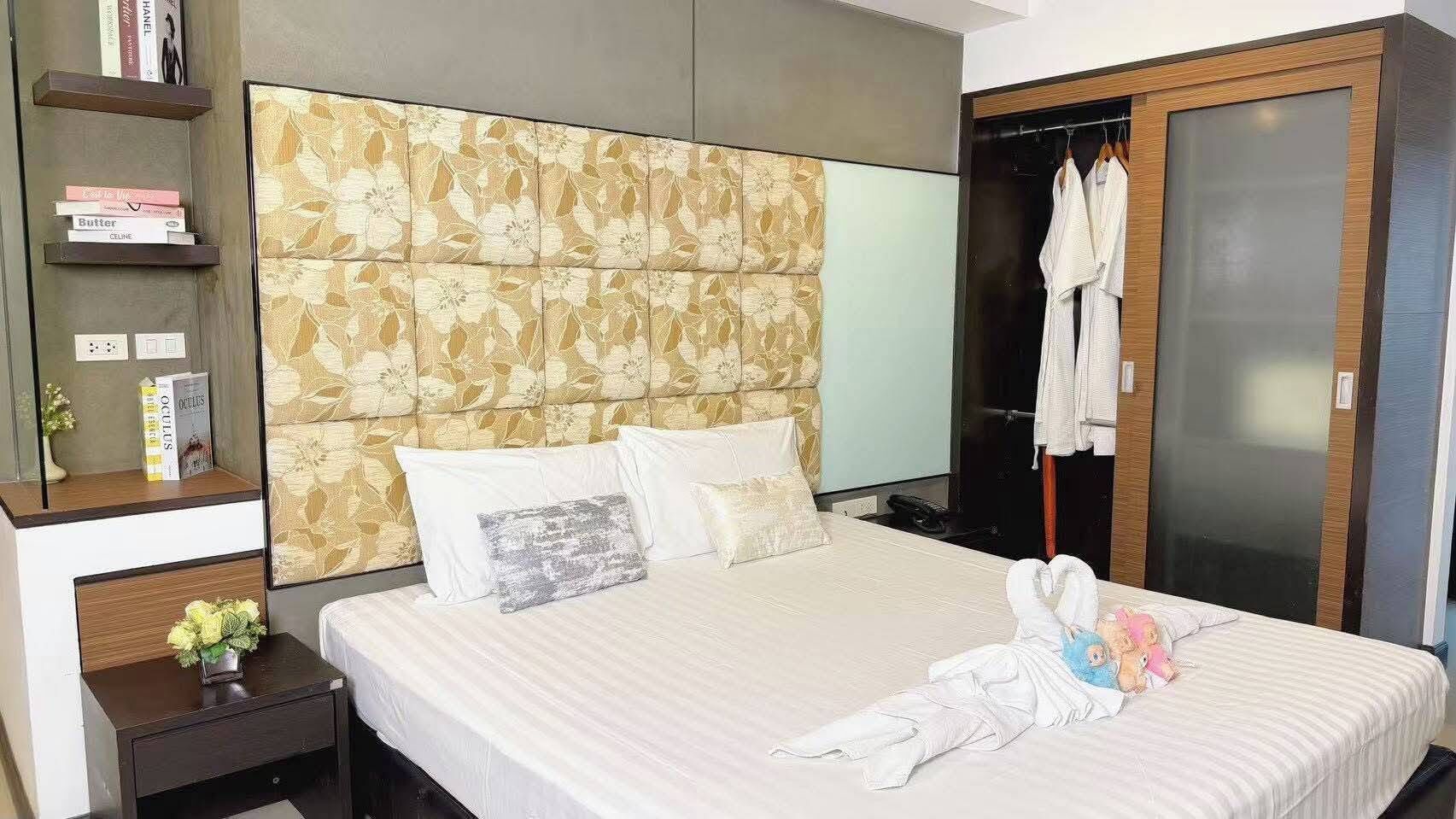 A hotel room with a bed, a wardrobe, a nightstand, and a shelf with books.