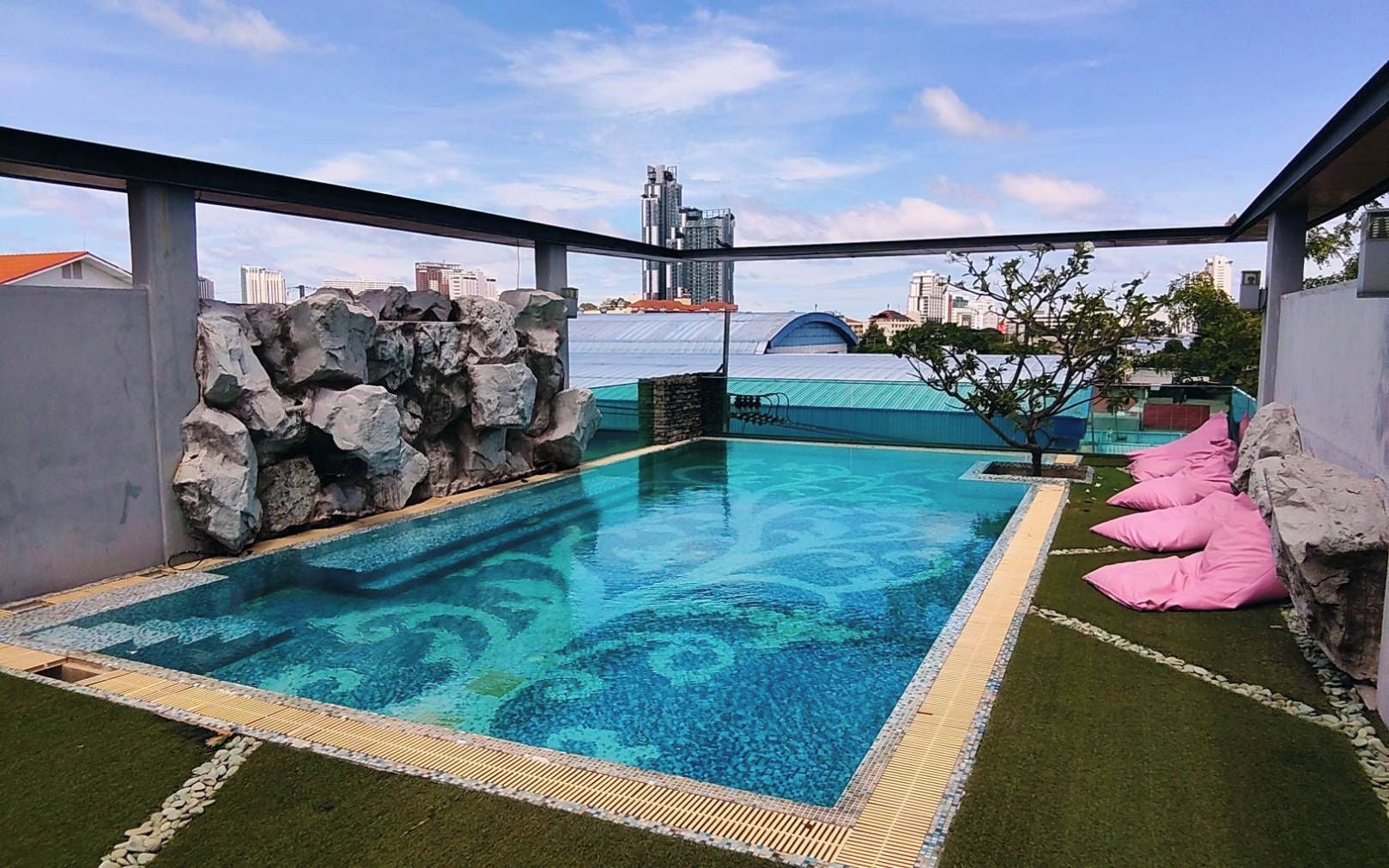 Una piscina en la azotea con un elemento acuático de agua azul cristalina, rodeada por un muro de piedra y una zona ajardinada.