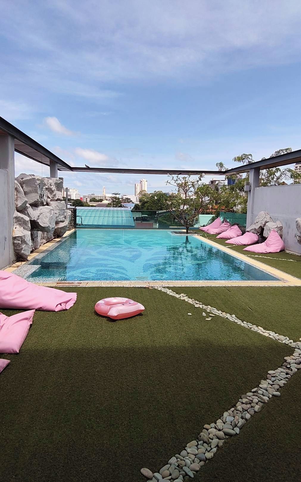 A swimming pool with artificial grass and rocks, surrounded by a metal fence.
