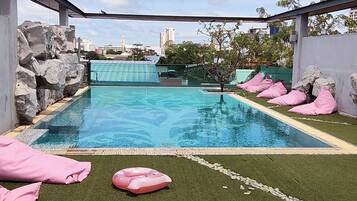 A swimming pool with artificial grass and rocks, surrounded by a metal fence.