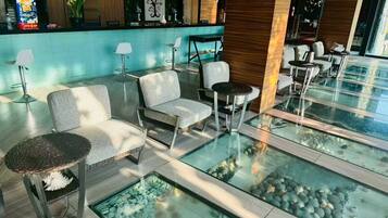 A modern lobby with seating areas, a reception desk, and a glass fish pond.