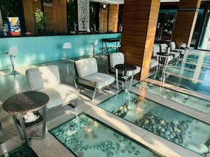 A modern lobby with seating areas, a reception desk, and a glass fish pond. - Starlight Hotel Pattaya  Le Vernissage (Bang Lamung)