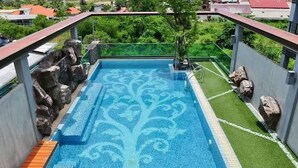 Una piscina en la azotea con un diseño decorativo, rodeada de rocas y un pequeño árbol.