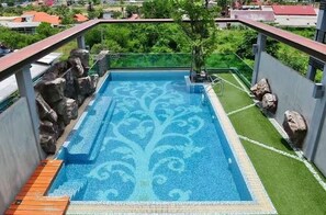 Una piscina gegantada a la teulada amb un dibuix decoratiu, envoltada de roques i un arbre petit.