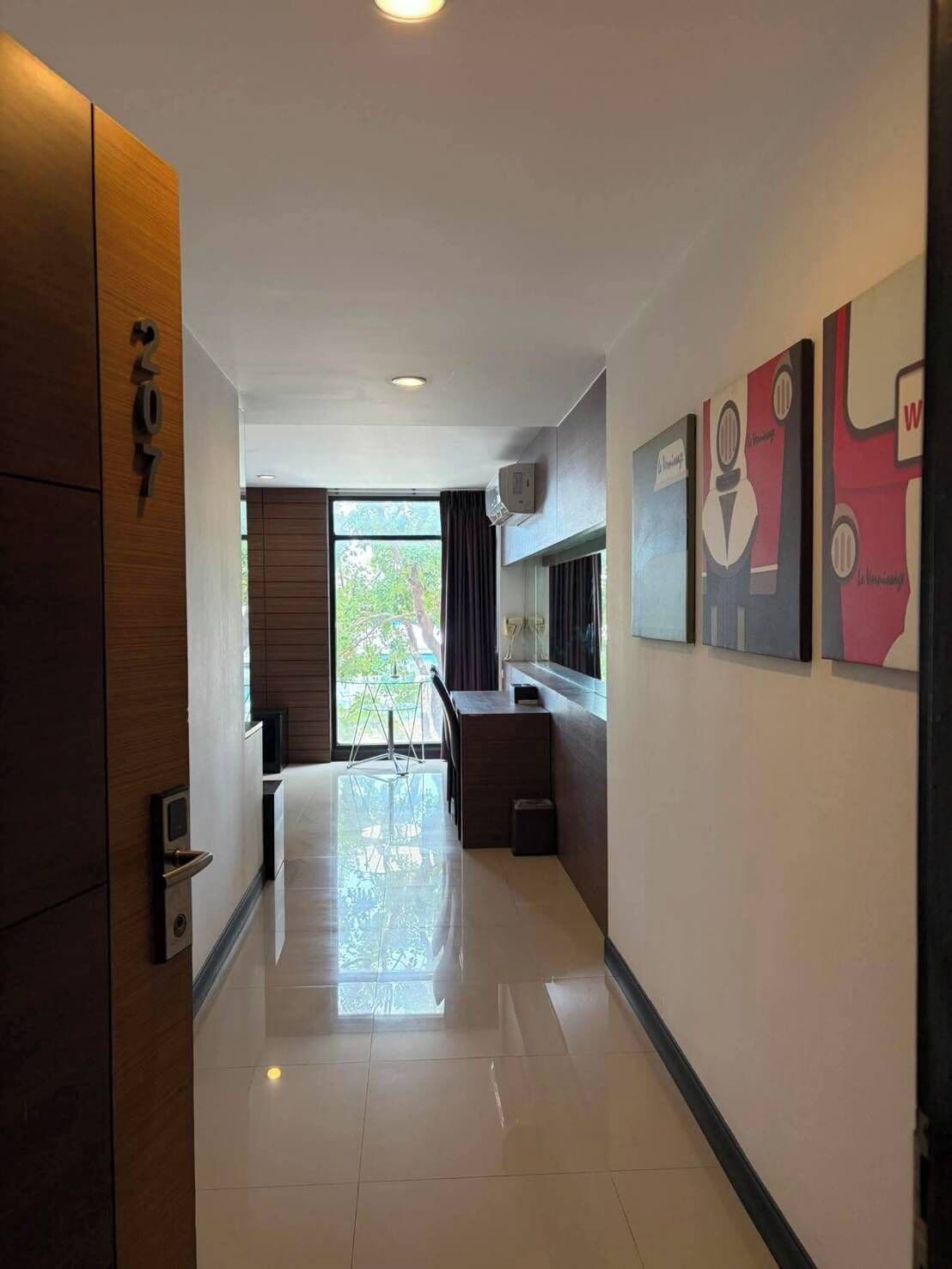 A hotel corridor with a wooden door, a dining area with a table and chairs, and artwork on the walls.
