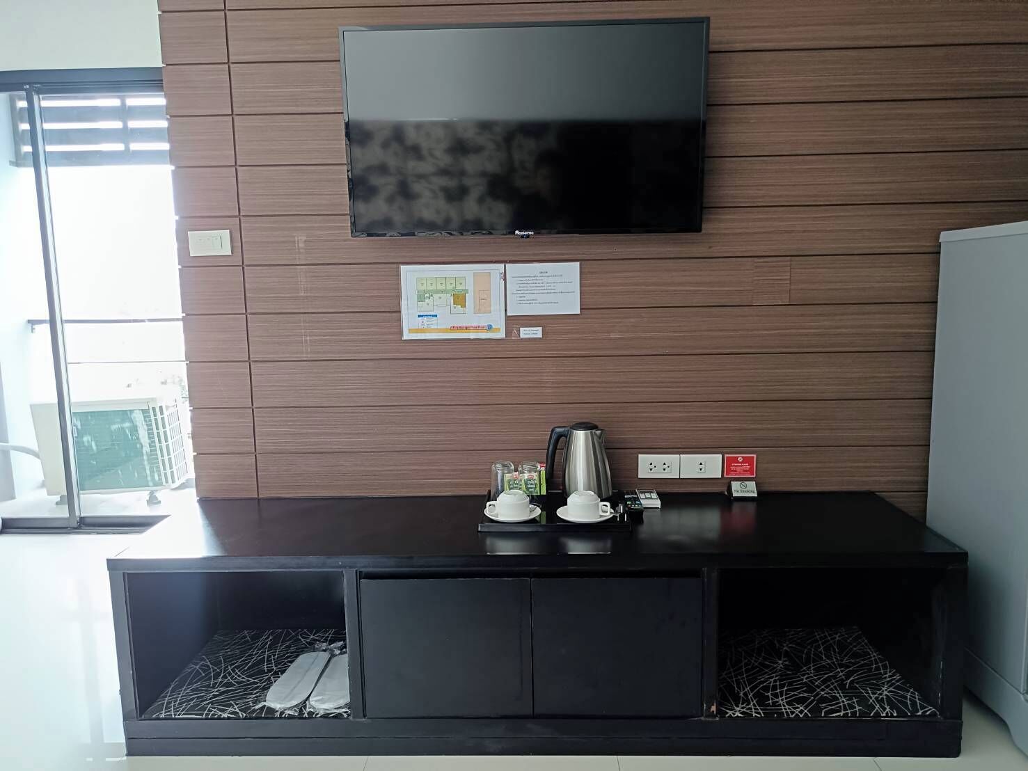 Una habitación moderna con una televisión de pantalla plana montada en una pared de madera, una estación de café y una pequeña zona de estar con un banco acolchado.