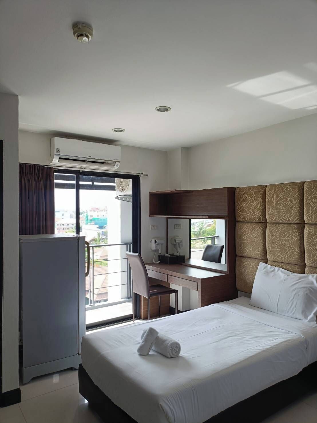 A hotel room with a bed, a desk, a chair, a minibar, and a view of the outside.