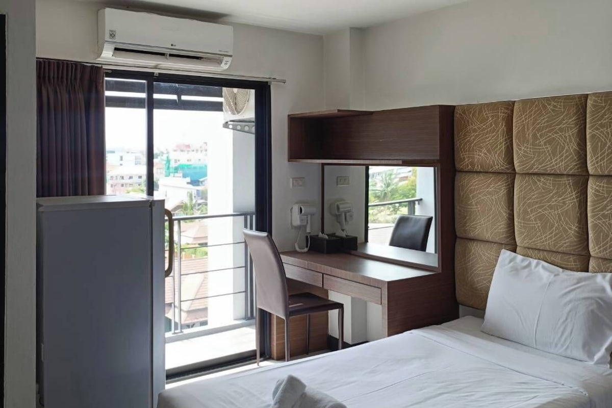 Una habitació d'hotel amb un llit, escriptori, cadira, barra minibar i vistes a l'exterior.