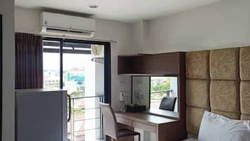 A hotel room with a bed, a desk, a chair, a minibar, and a view of the outside.
