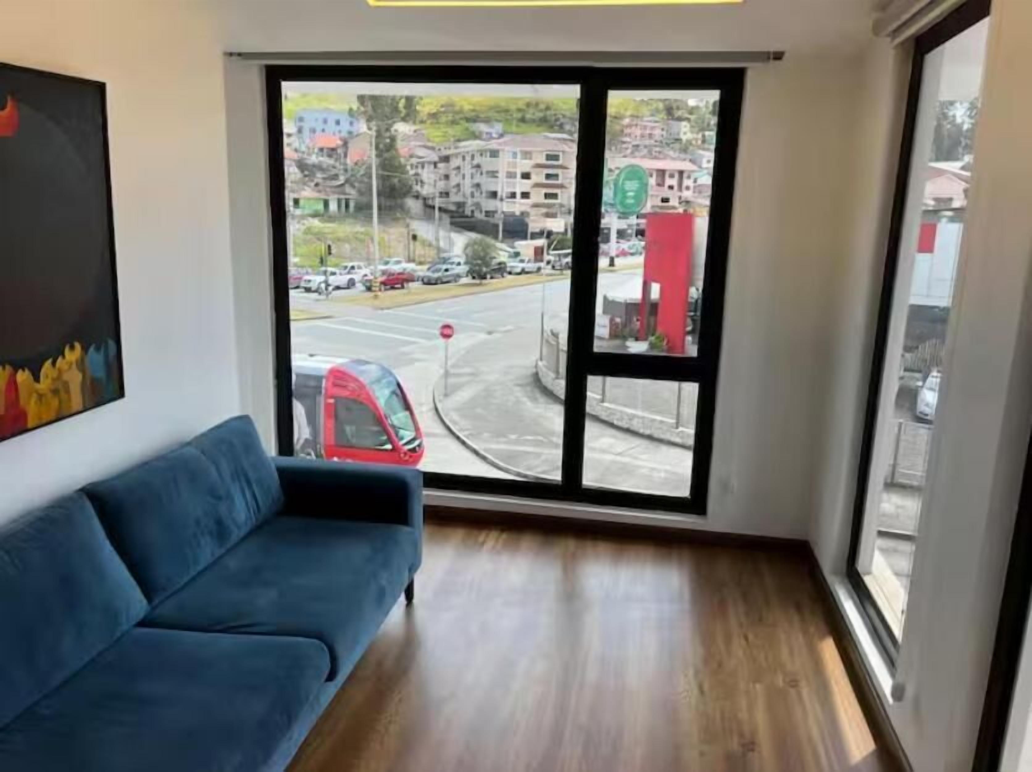 Una habitación con un sofá azul, un ventanal y vistas a una calle con coches.