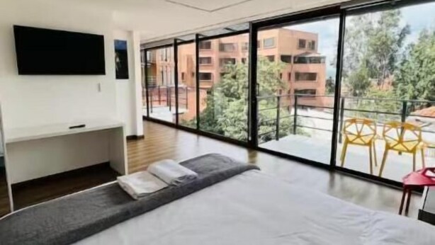 A modern hotel room with a large bed, a flat-screen TV, and a balcony with a view of the city.