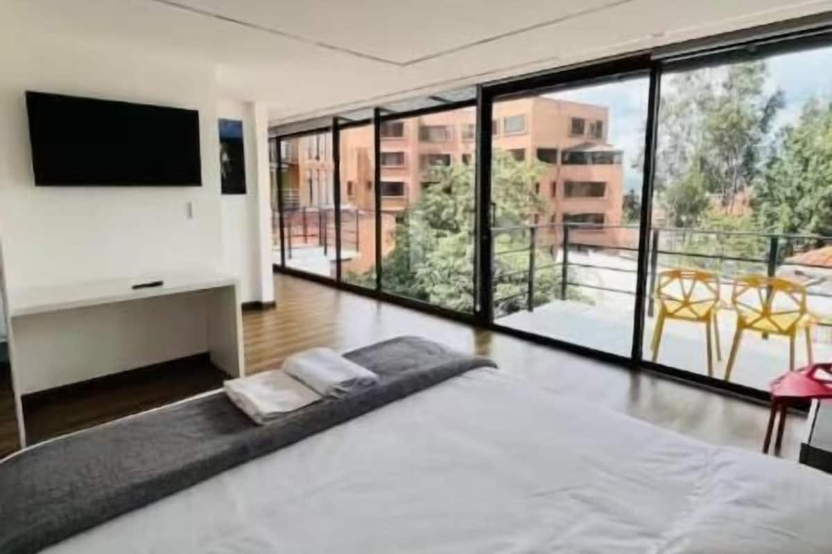 A modern hotel room with a large bed, a flat-screen TV, and a balcony with a view of the city.