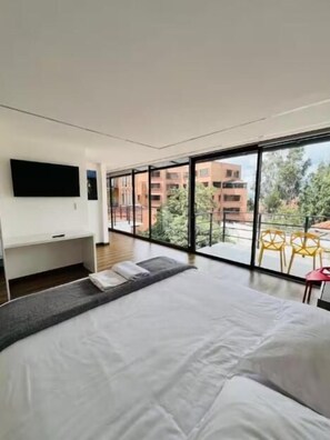 A modern hotel room with a large bed, a flat-screen TV, and a balcony with a view of the city. - Hotel Apartment Cuenca (Cuenca)