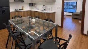 A modern kitchen with a glass dining table and chairs, wooden cabinets, and a built-in oven.