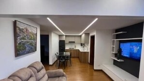 A modern living room with a sofa, a TV, and a kitchen in the background.
