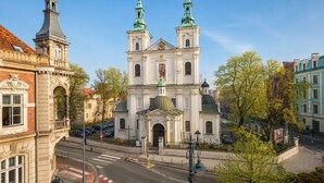 Eine historische Kirche mit zwei Türmen und einer zentralen Kuppel, umgeben von städtischen Gebäuden und blauem Himmel.