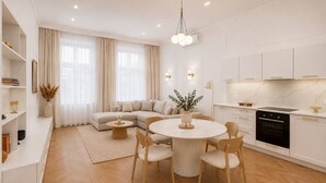 Ein modernes Wohnzimmer mit einer Couch, einem Esstisch mit Stühlen, einer Küchenzeile mit Herd und einem großen Fenster mit Vorhängen.