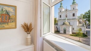 Una ventana que muestra una iglesia blanca con cúpulas verdes y una pequeña torre con campana.