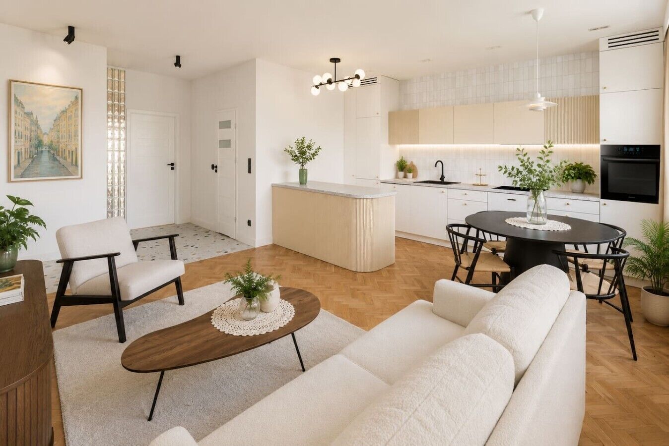 Un salon moderne avec un canapé, une table basse et des fauteuils, une cuisine avec un coin repas, et un tableau accroché au mur.