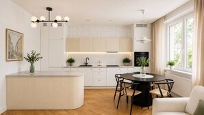 Een moderne keuken met een centraal eiland, een eetgedeelte met een ronde tafel en uitzicht op de natuur door grote ramen.