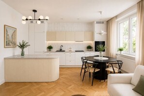 Eine moderne Küche mit einer zentralen Kochinsel, einem Essbereich mit rundem Tisch und Blick ins Freie durch große Fenster.