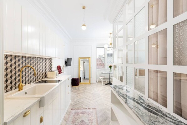 A modern kitchen with white cabinetry, a herringbone floor pattern, a marble countertop, and a large window with a view. - Royal Residence • (3 x Suites) • Main Sq • 9 Guest (Kraków)