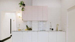 Et moderne køkken med hvide skabe, en marmor bordplade, en vask med en guldfarvet hane og en lille plante på væggen.