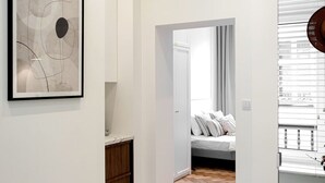 Ein Flur, der in ein Schlafzimmer mit einem Bett, einem Holzschrank und einem Wandbild mit abstrakter Kunst führt.
