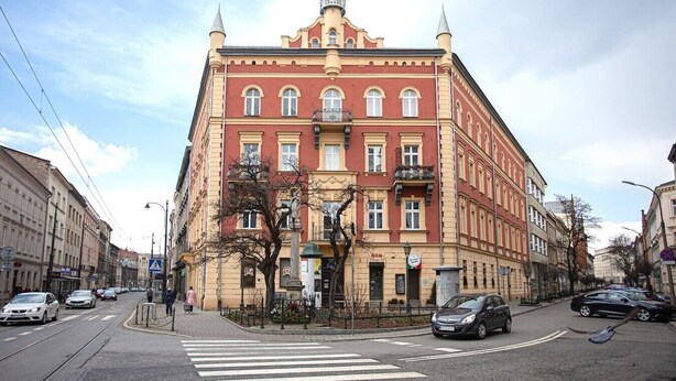 Ein mehrgeschossiges Gebäude mit roter Fassade, großen Fenstern und einer Ecklage mit Blick auf die Straße.