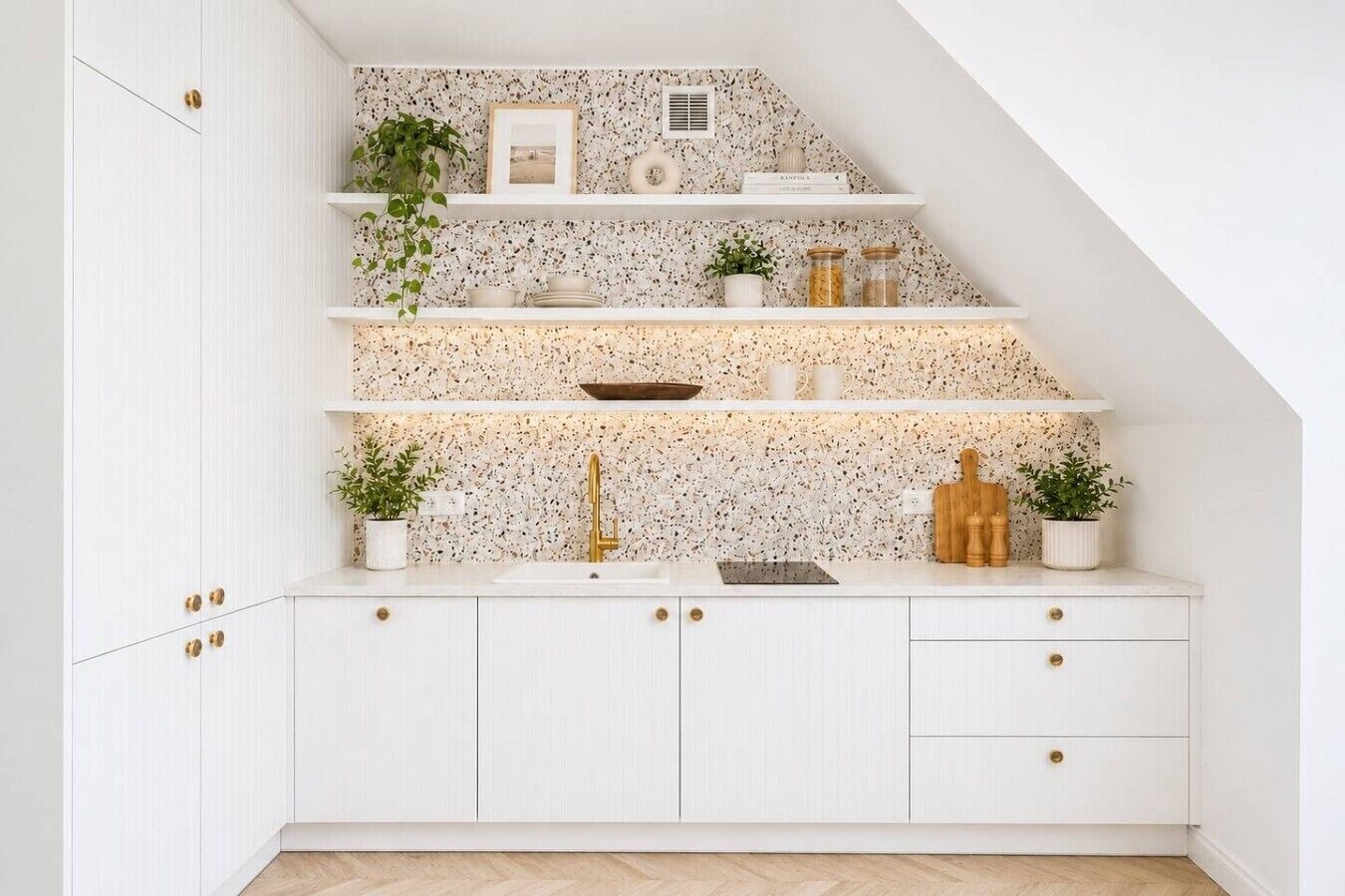 Una cocina con armarios blancos, salpicadero con motivo de espiga y una escalera de madera.