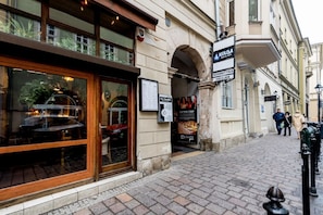 A street view with a restaurant entrance, a sign for 'KOLBA RESTO-BAR,' and a pedestrian walkway. - Secret Studio at Main Square D2 (Kraków)
