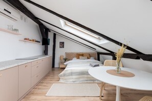 Ein Schlafzimmer mit schrägverdeckter Decke, einem Bett, Nachttischen und einem Fenster.