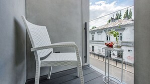 En vit flätstol på en balkong, med ett litet bord och en vas med blommor.