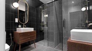 Un baño moderno con tocador de madera, un espejo grande y mampara de ducha con puerta de vidrio perforado.