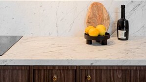 Una cocina con encimera de mármol, un cuenco de madera con limones, una botella de vino y una lámpara de pared.
