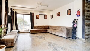 A living room with a sectional sofa, a flat-screen TV, a ceiling fan, and a fire extinguisher on the wall. - Super Townhouse Taj Mahal East Gate (Agra)
