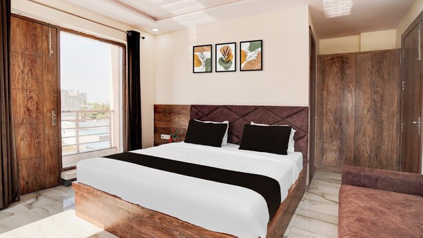 A modern bedroom with a wooden bed frame, a large window, and a view of the city. - Super Townhouse Taj Mahal East Gate (Agra)