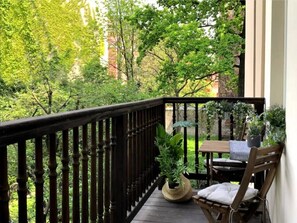 A wooden balcony with a black railing, a wooden table with a chair, and potted plants. - Majestic Suite • 1BR • Main Sq. 3 min • Elevator (Kraków)
